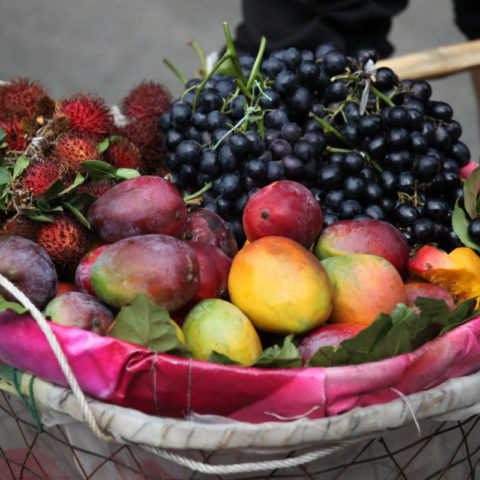 Uliczny sprzedawca owoców w Chinach. W koszyku ma rambutany, mango, śliwki i winogrona